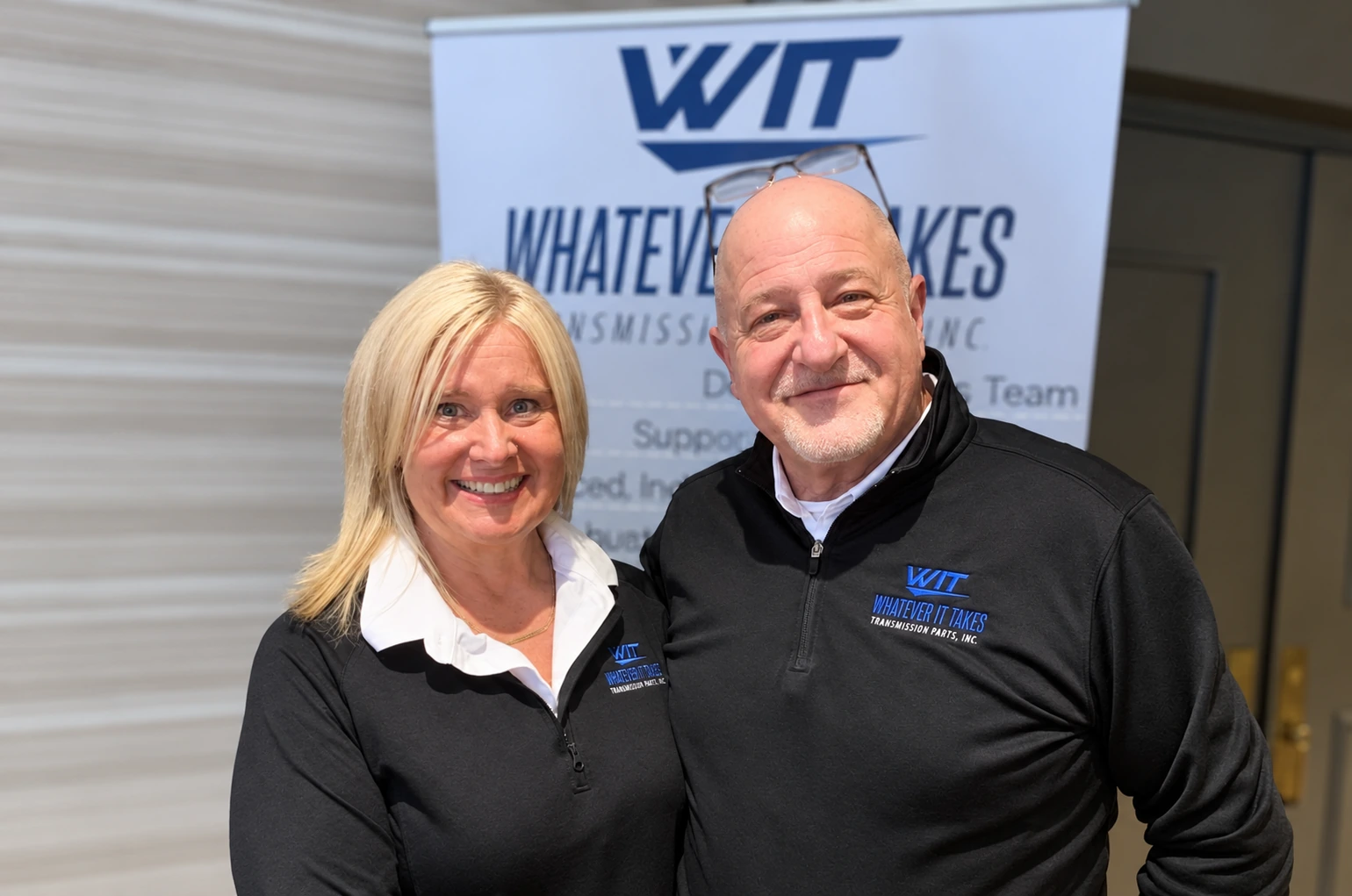 Two people wearing WIT shirts in front of a WIT banner.