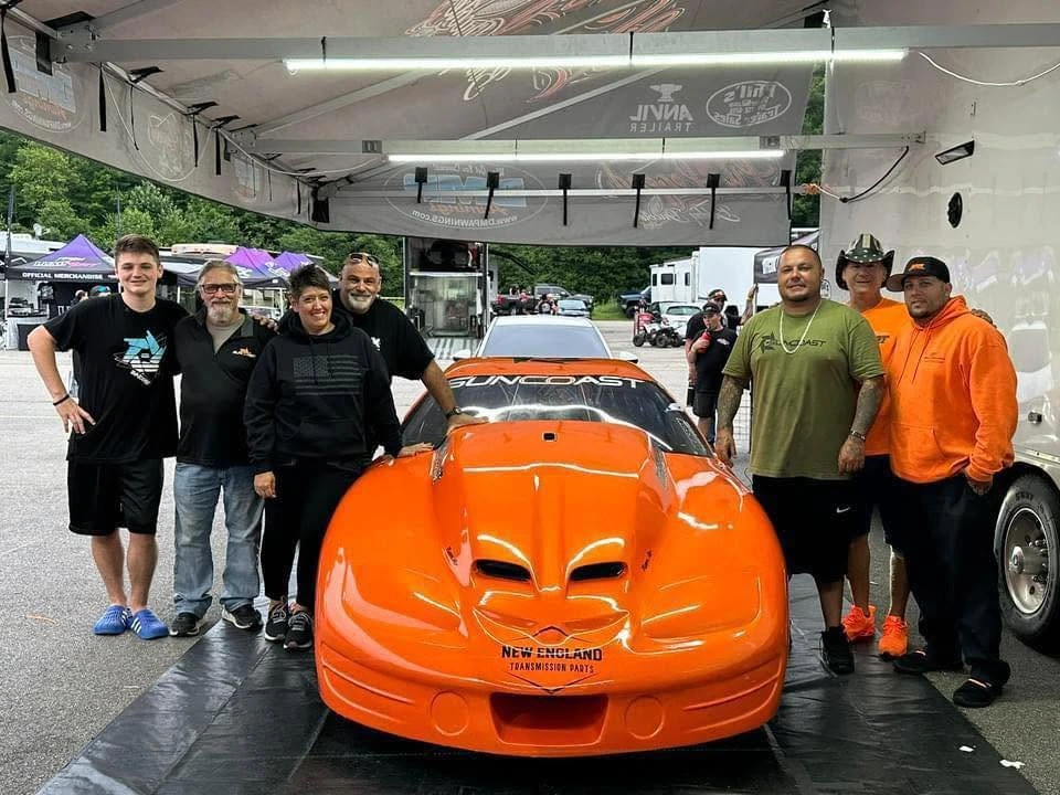 Group beside an orange SunCoast race car displaying New England Transmission Parts branding.